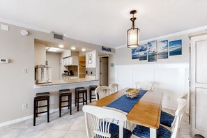 Enjoy meals with friends and family in this spacious dining area, featuring a long table and modern kitchen.