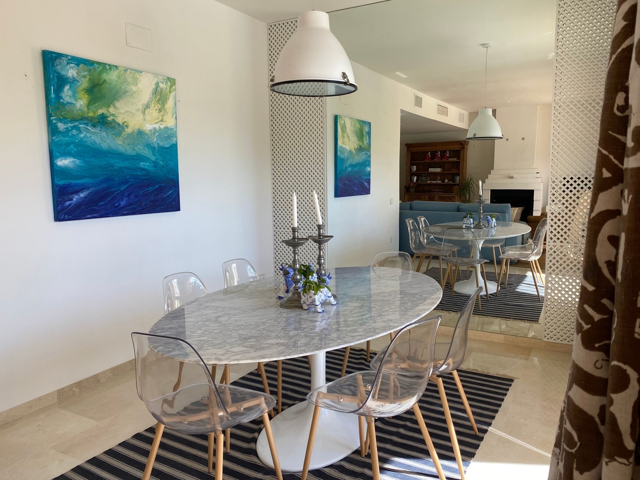 Un comedor con una mesa redonda, sillas transparentes, un papel tapiz estampado y pinturas abstractas.