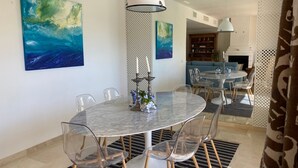 Un espace repas avec une table ronde, des chaises transparentes, un mur à motifs et des tableaux abstraits.