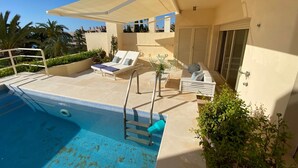 Un espace piscine aménagé sur le toit, avec des chaises longues, une table et un coin salon abrité.
