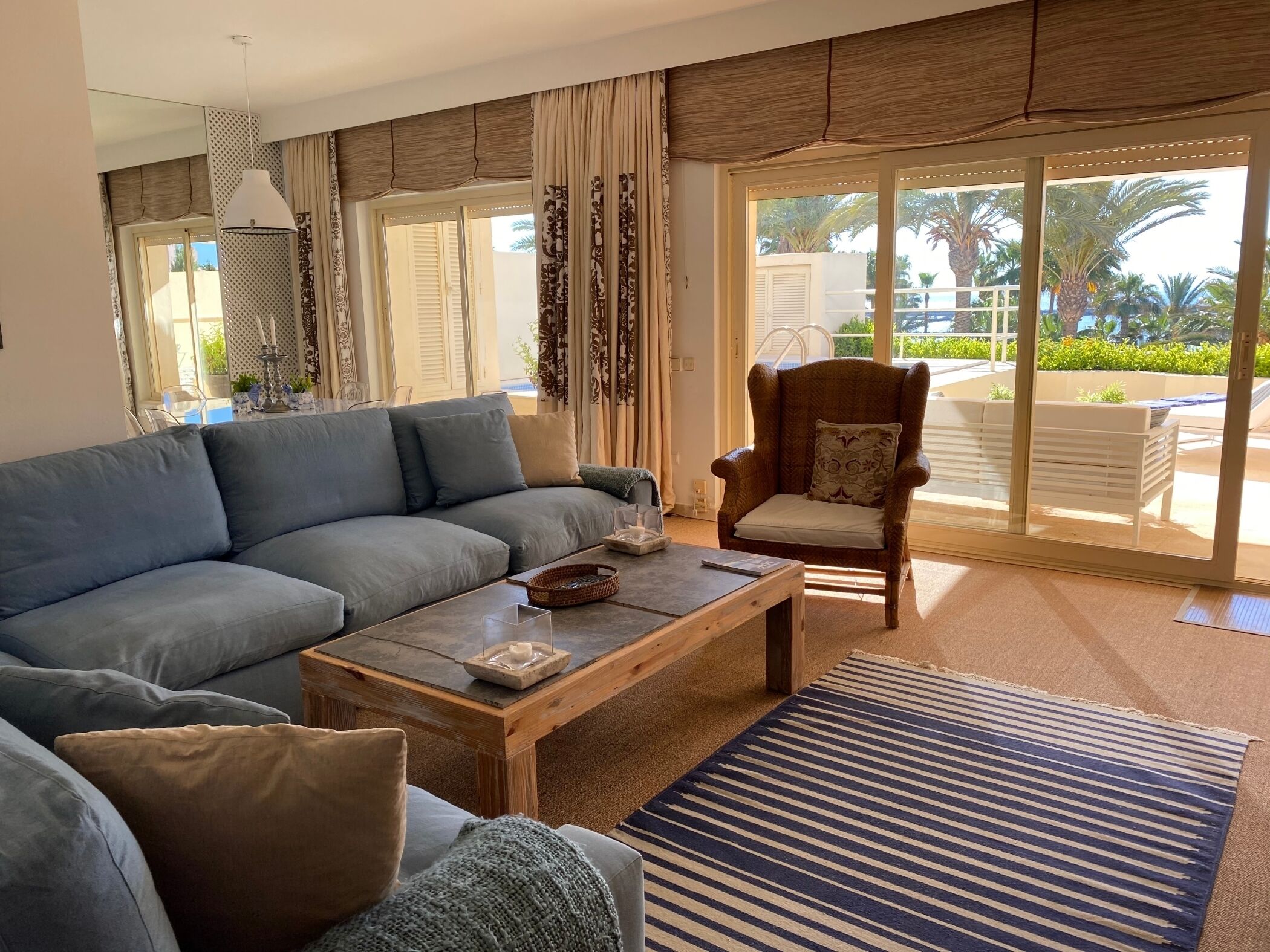 Una sala de estar con sofá, sillón, mesa de centro y vistas a una piscina y palmeras.
