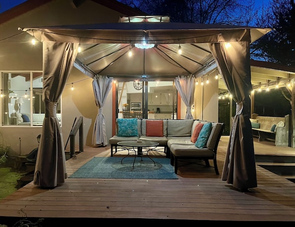 Un patio exterior con una zona de estar techada, una mesa de comedor y vistas al interior de la casa.