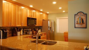 A kitchen with wooden cabinets, granite countertops, stainless steel appliances, and a wall-mounted sign. - BEAUTIFUL DIRECT OCEANFRONT VIEW NOW RENTING FALL-SPRING WATCH ROCKET LAUNCHES! (Cocoa Beach)
