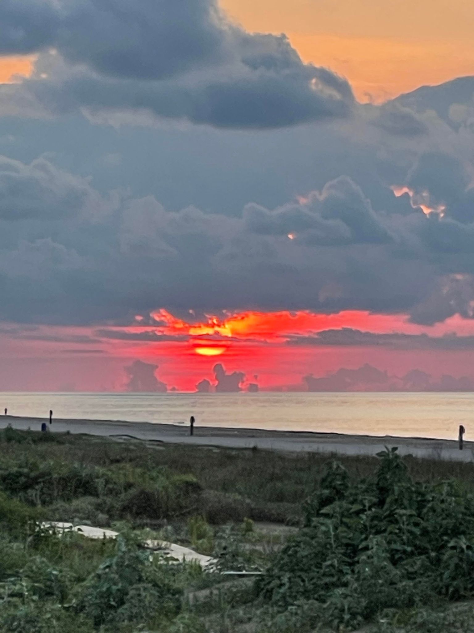 A sunset over a coastal landscape with a clear sky and distant mountains.
