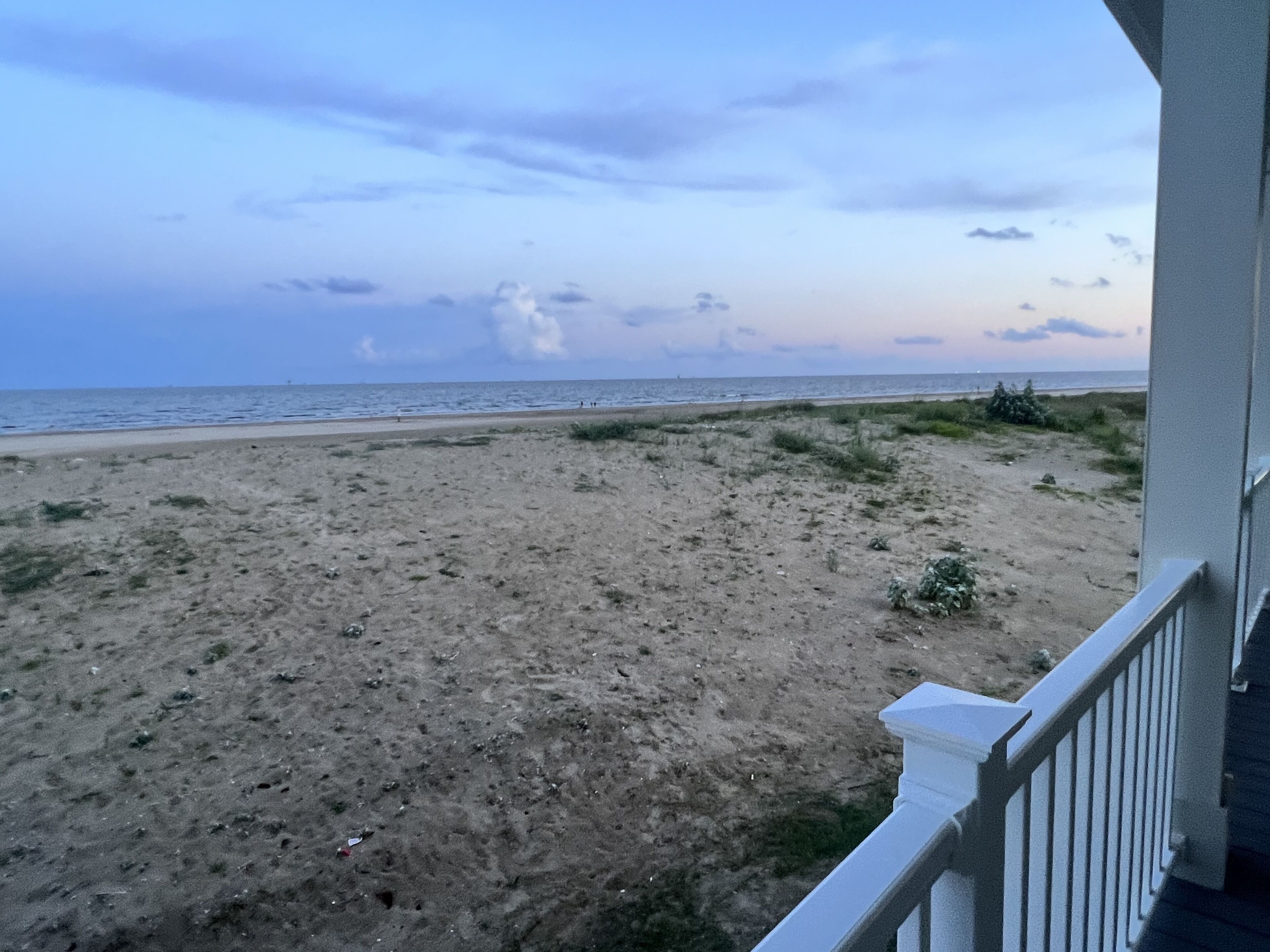 Blick auf einen Strand vom Balkon mit Geländer, Sandstrand und Meer im Hintergrund.