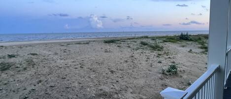 Blick auf einen Strand vom Balkon mit Geländer, Sandstrand und Meer im Hintergrund.