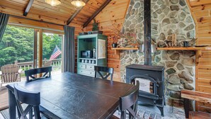 Ein Holzblockhaus im Inneren mit einem Kamin aus Stein, einem Esstisch mit Stühlen und Blick ins Freie.
