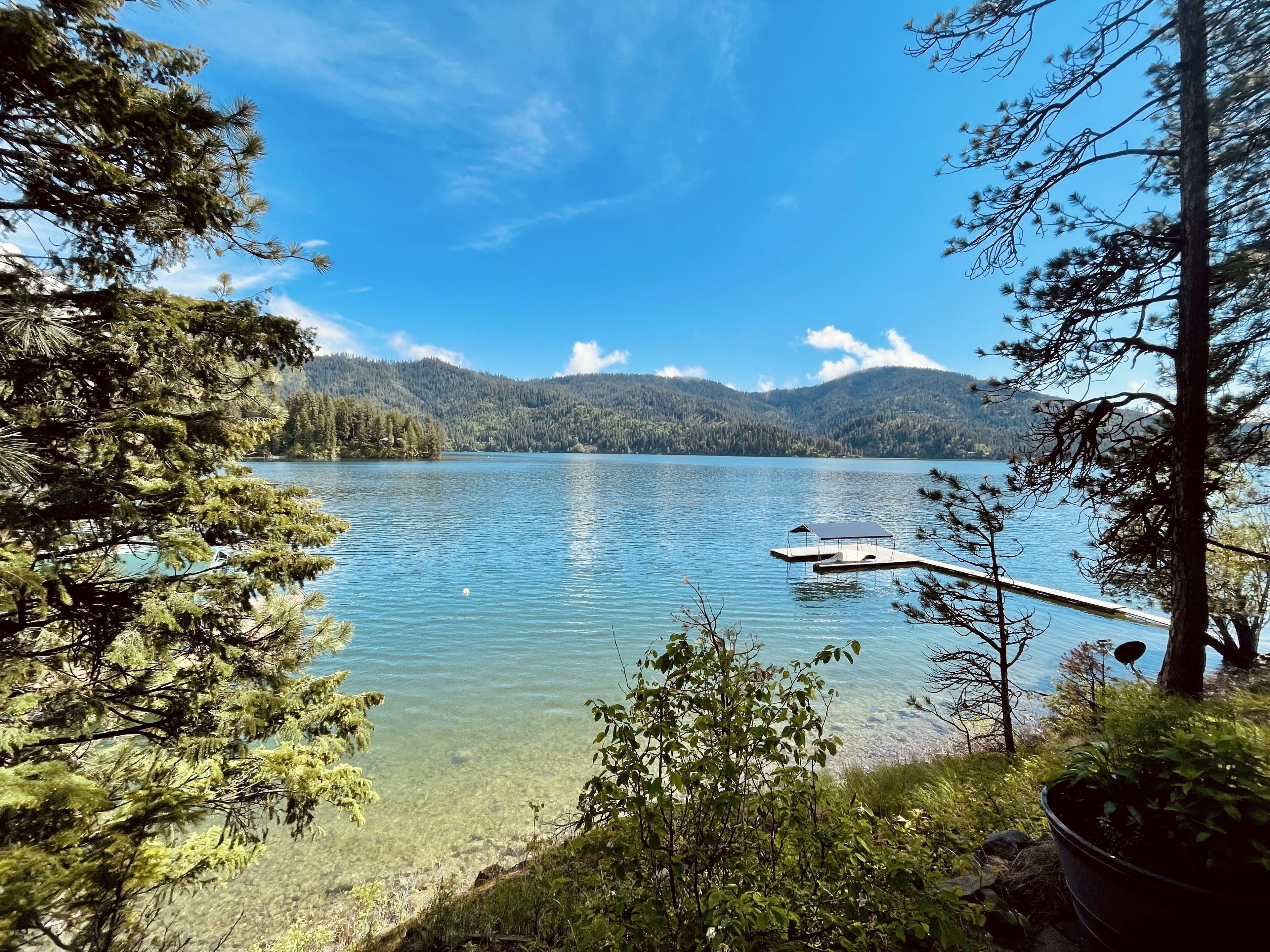Una vista limpida di un lago circondato da montagne e alberi, con un molo che si protende nell'acqua.