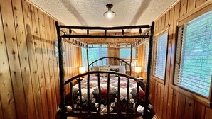 A wooden-paneled room with a four-poster bed, a window with blinds, and a lamp on a bedside table. - Pine View Cabin: Rustic Hayden Lake Cabin with Bunkhouse and Private Dock (Hayden)