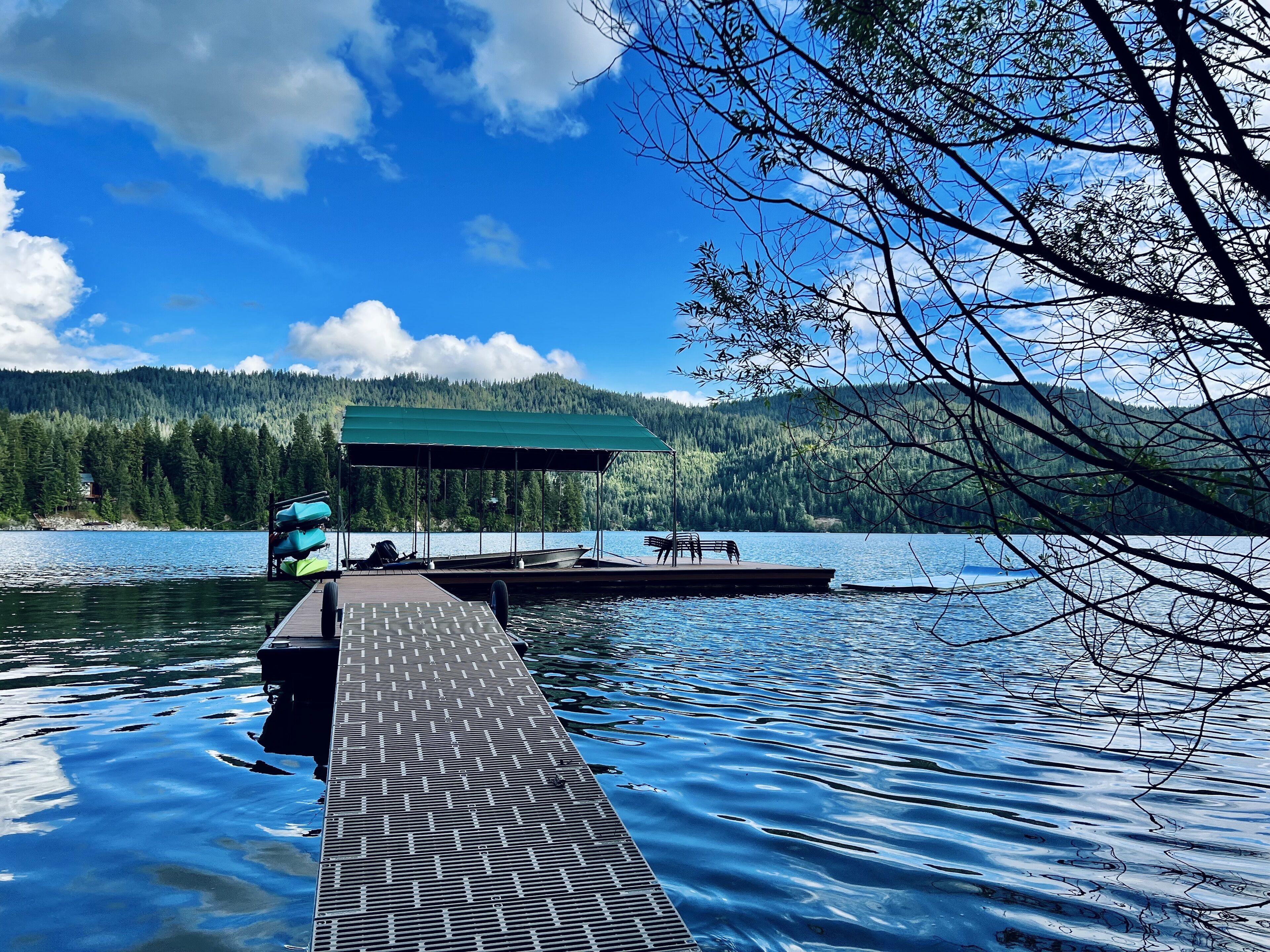 A wooden dock extending into a calm lake with a covered seating area and kayaks.