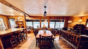 A wooden interior with a central dining table, bar area, and seating. - Pine View Cabin: Rustic Hayden Lake Cabin with Bunkhouse and Private Dock (Hayden)