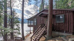 A cabin with a staircase leading to a deck overlooking a lake, surrounded by trees. - Pine View Cabin: Rustic Hayden Lake Cabin with Bunkhouse and Private Dock (Hayden)