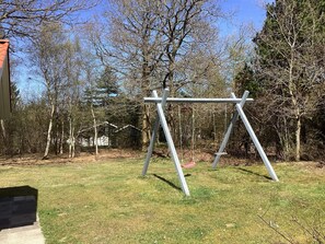 A swing set in a grassy yard with trees and a house in the background. - Holiday Home in NÃ¸rre Nebel (Norre Nebel)