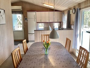 A dining area with a table, chairs, a vase with flowers, and a kitchen in the background. - Holiday Home in NÃ¸rre Nebel (Norre Nebel)
