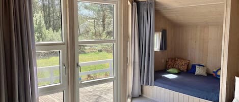 A room with a large sliding glass door leading to a deck, a bed with pillows, and a small table.
