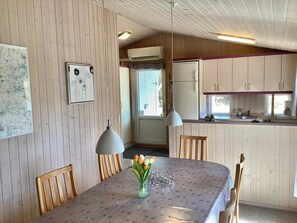 A dining area with a table, chairs, a vase with flowers, and a kitchen in the background. - Holiday Home in NÃ¸rre Nebel (Norre Nebel)