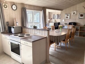 A compact kitchen with a stove, microwave, and a dining area with chairs and a table. - Holiday Home in NÃ¸rre Nebel (Norre Nebel)