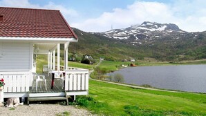 A house with a red-tiled roof, a porch with white railings, and a view of a lake and mountains in the background. - Holiday Home in Leknes (Vestvågøy)