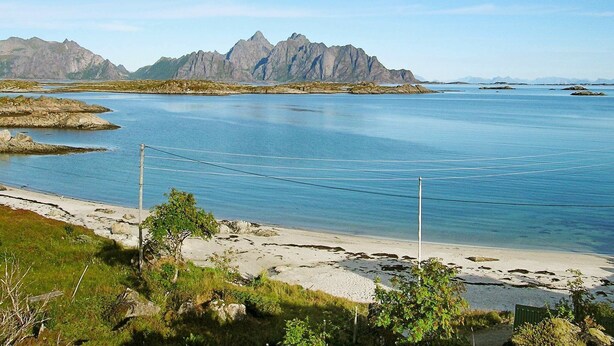 A coastal landscape with a beach, clear blue water, and distant mountains. - Holiday Home in Leknes (Vestvågøy)