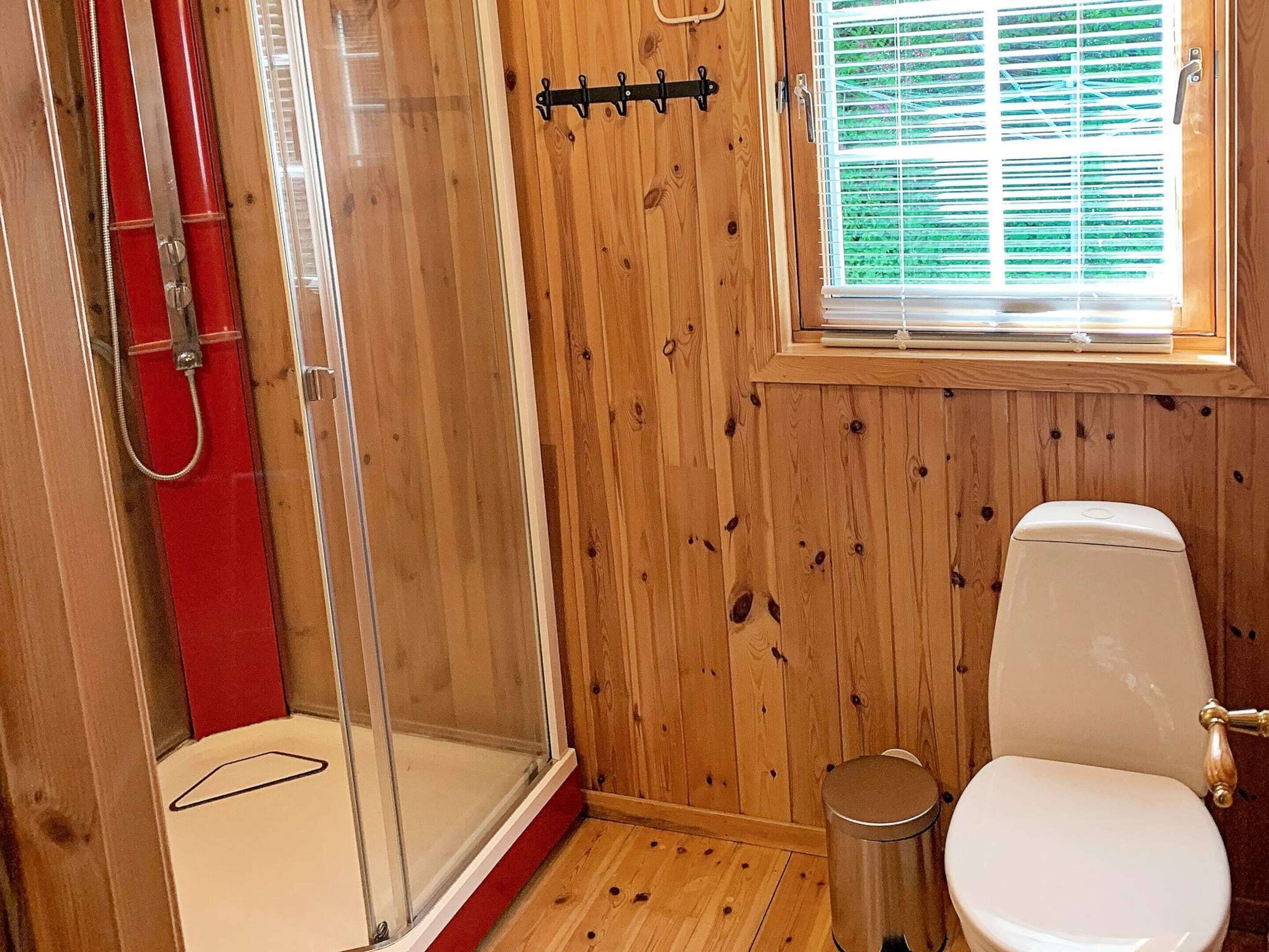 Un baño con paneles de madera, ducha, inodoro y ventana con persianas.