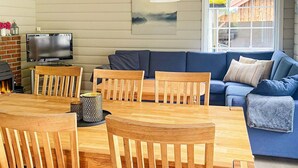 Ein gemütliches Wohnzimmer mit Esstisch aus Holz, Stühlen, einem blauen Sofa und einem Fernseher.