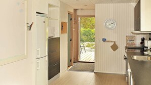 Une cuisine équipée d’un réfrigérateur, d’un four à micro-ondes et d’un évier. Une porte en bois donne accès à un espace extérieur où se trouve une chaise.