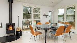 Un espace repas moderne avec une table en verre, des chaises en métal et un poêle à bois noir.