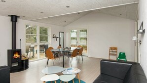Un vaste espace de vie doté d’une cheminée, d’une table à manger avec des chaises, d’un canapé noir et d’un tapis bleu.
