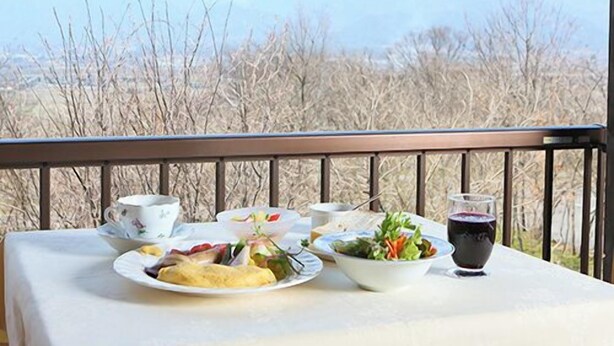 A table set with breakfast items including eggs, a salad, and a drink, overlooking a mountainous landscape. - Auberge Meiyanoki (Ikeda)