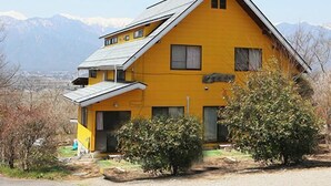 A yellow house with a gabled roof, surrounded by mountains and sparse vegetation. - Auberge Meiyanoki (Ikeda)