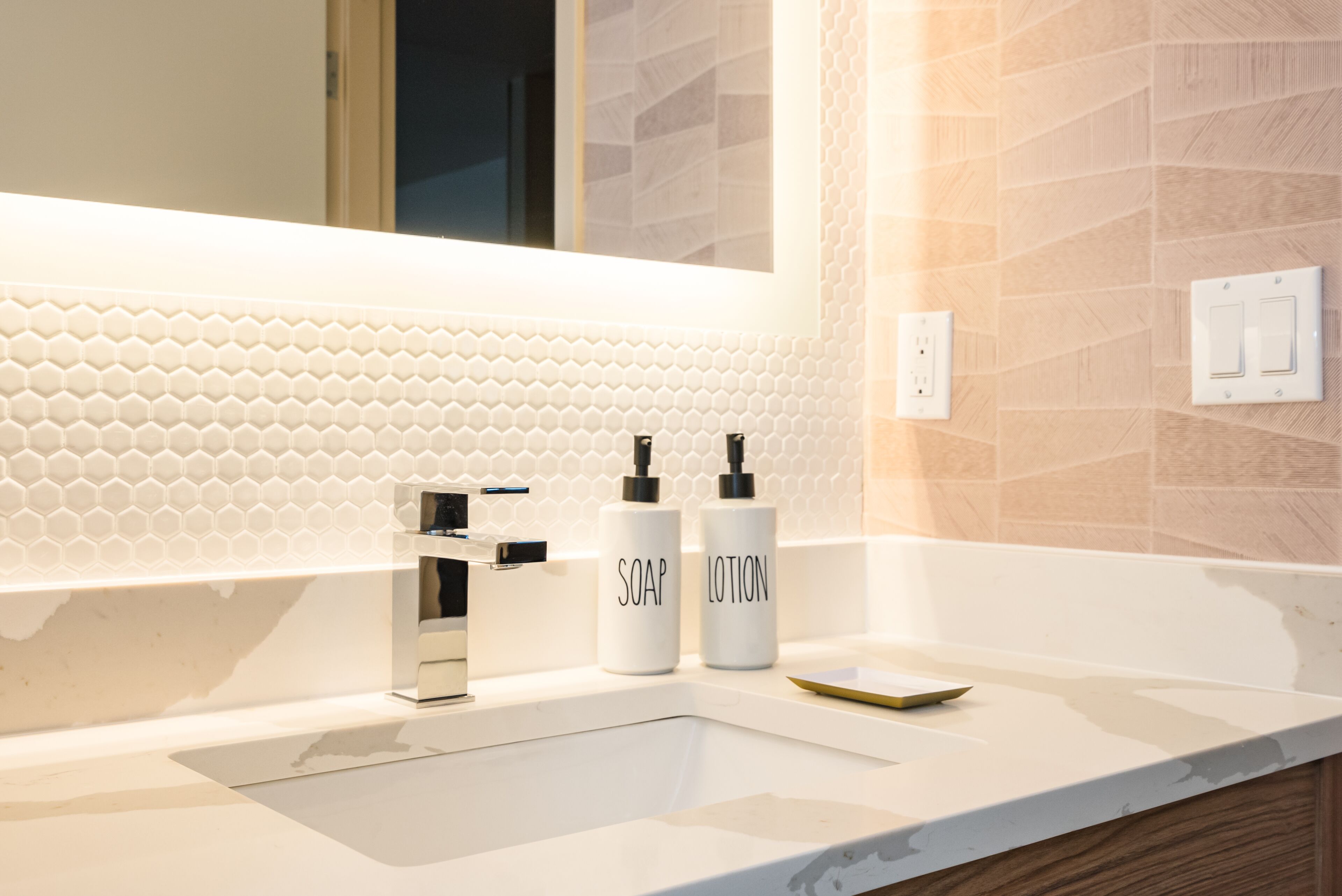 Een moderne badkamer met een witte wasbak, een spiegel en twee flessen met de tekst 'ZEEP' en 'LENGTEZUUR'.