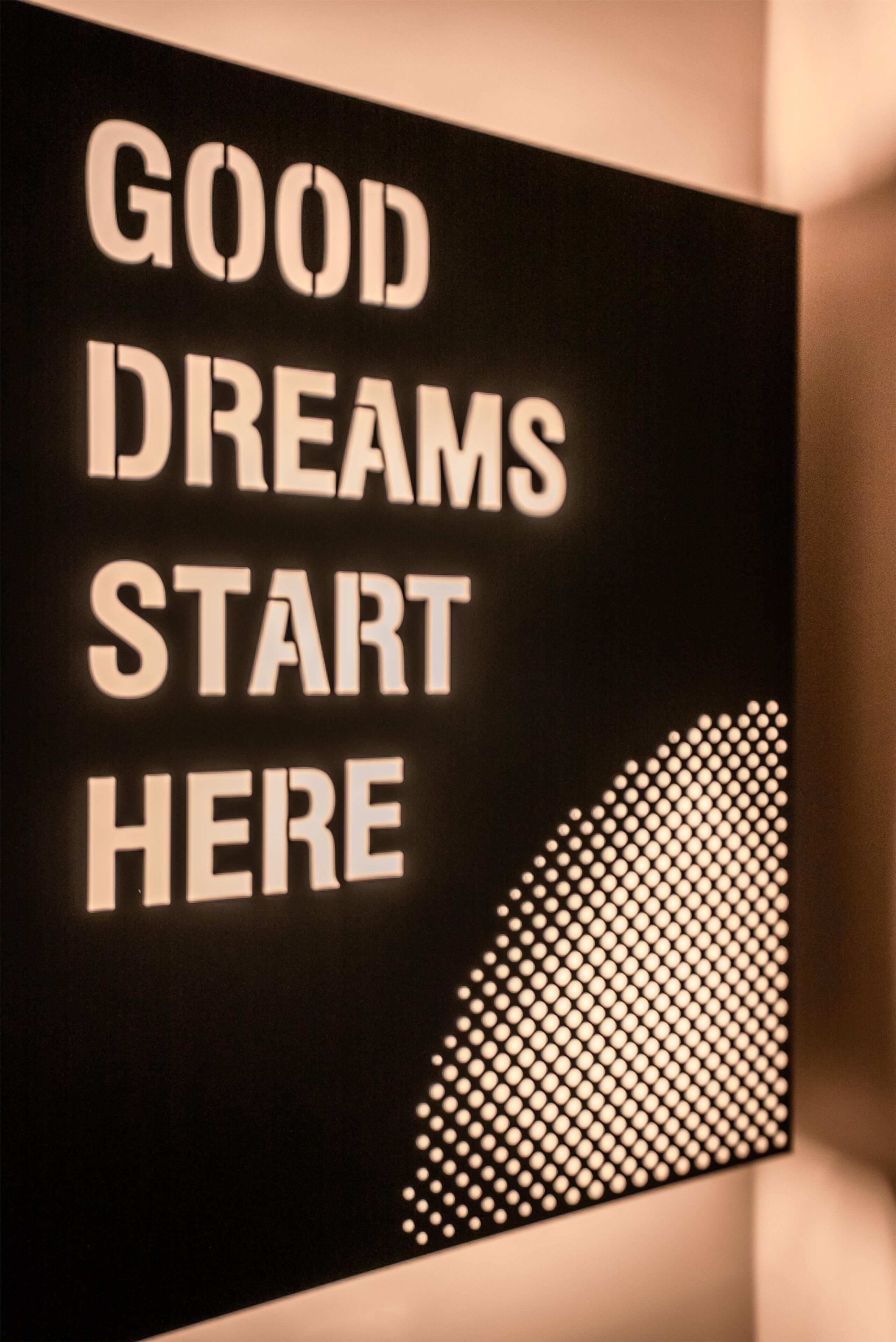 Un segnale con la scritta "GOOD DREAMS START HERE" in un font luminoso e marcato.