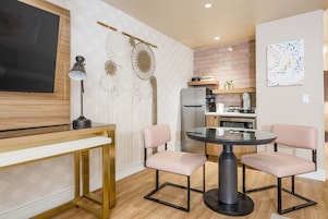 Una cocina moderna con refrigerador, microondas y armarios de madera. Hay una mesa de comedor con dos sillas y un televisor montado en la pared.