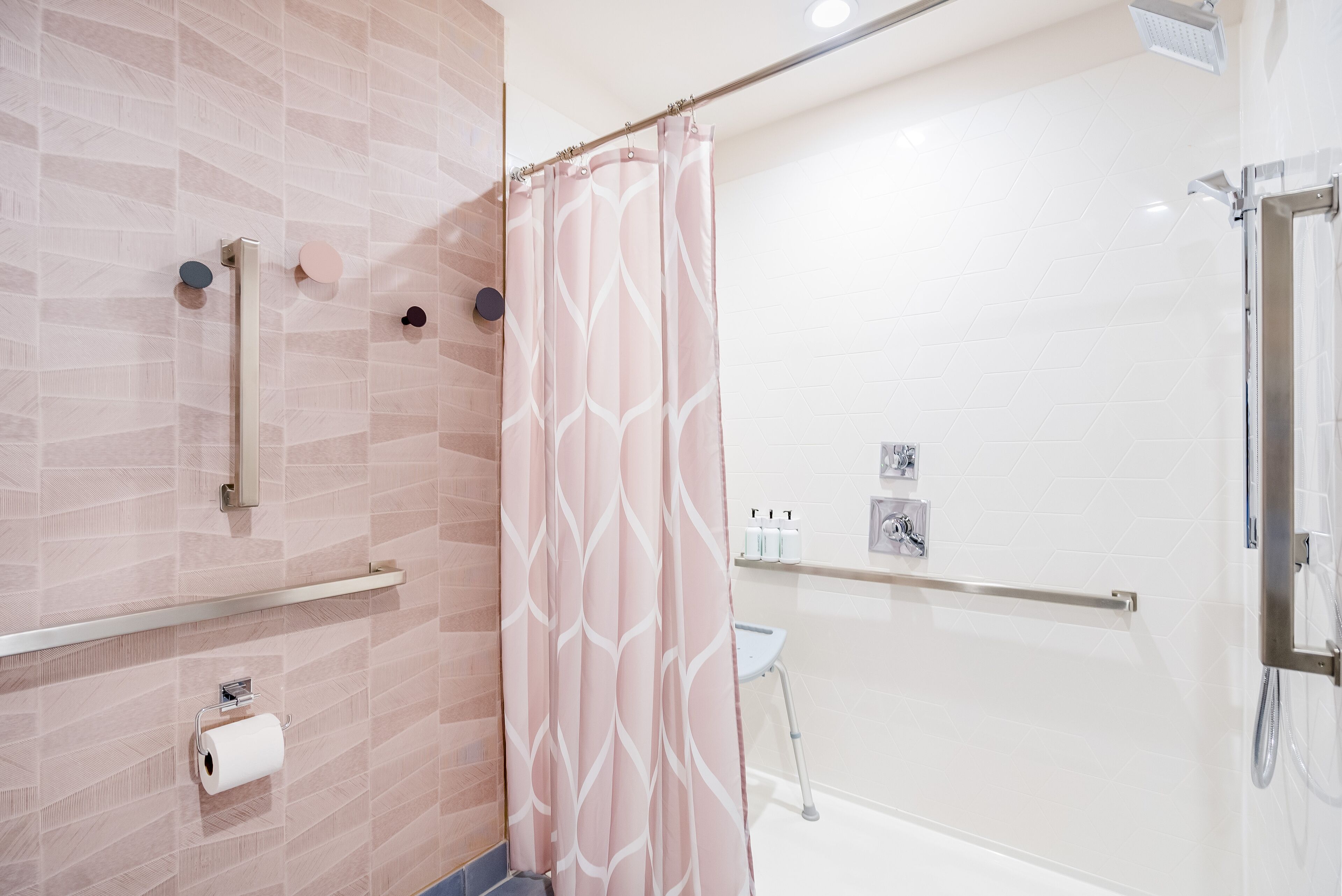 A modern bathroom with a shower, toilet paper, and hand sanitizer.