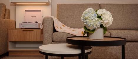 A modern living room with a sofa, a round coffee table, a side table with a Crosley radio, and a vase with flowers.