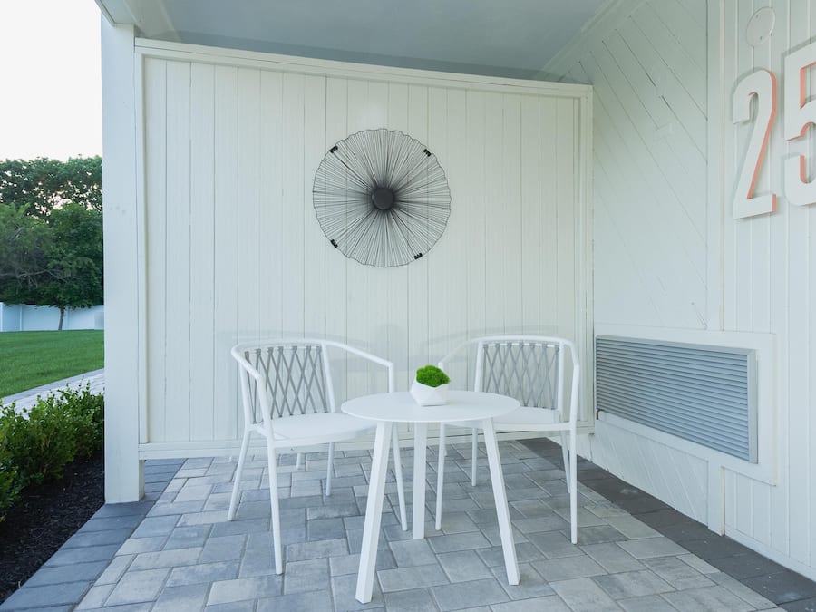 En vit uteplats med två vita stolar och ett bord, ett dekorativt parasoll och en vägg med siffran 25.