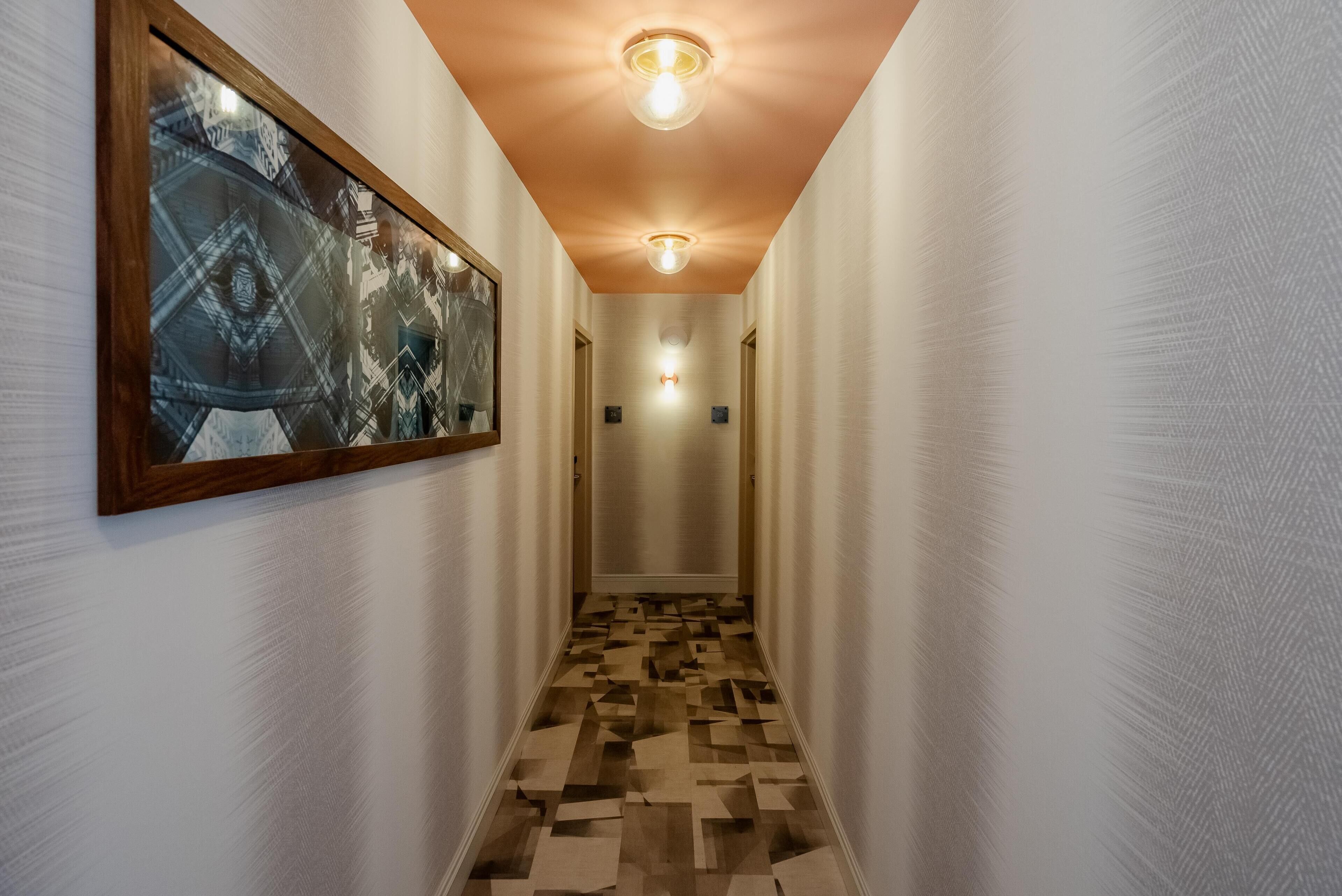 A hallway with a patterned floor, framed artwork on the wall, and ceiling lights.