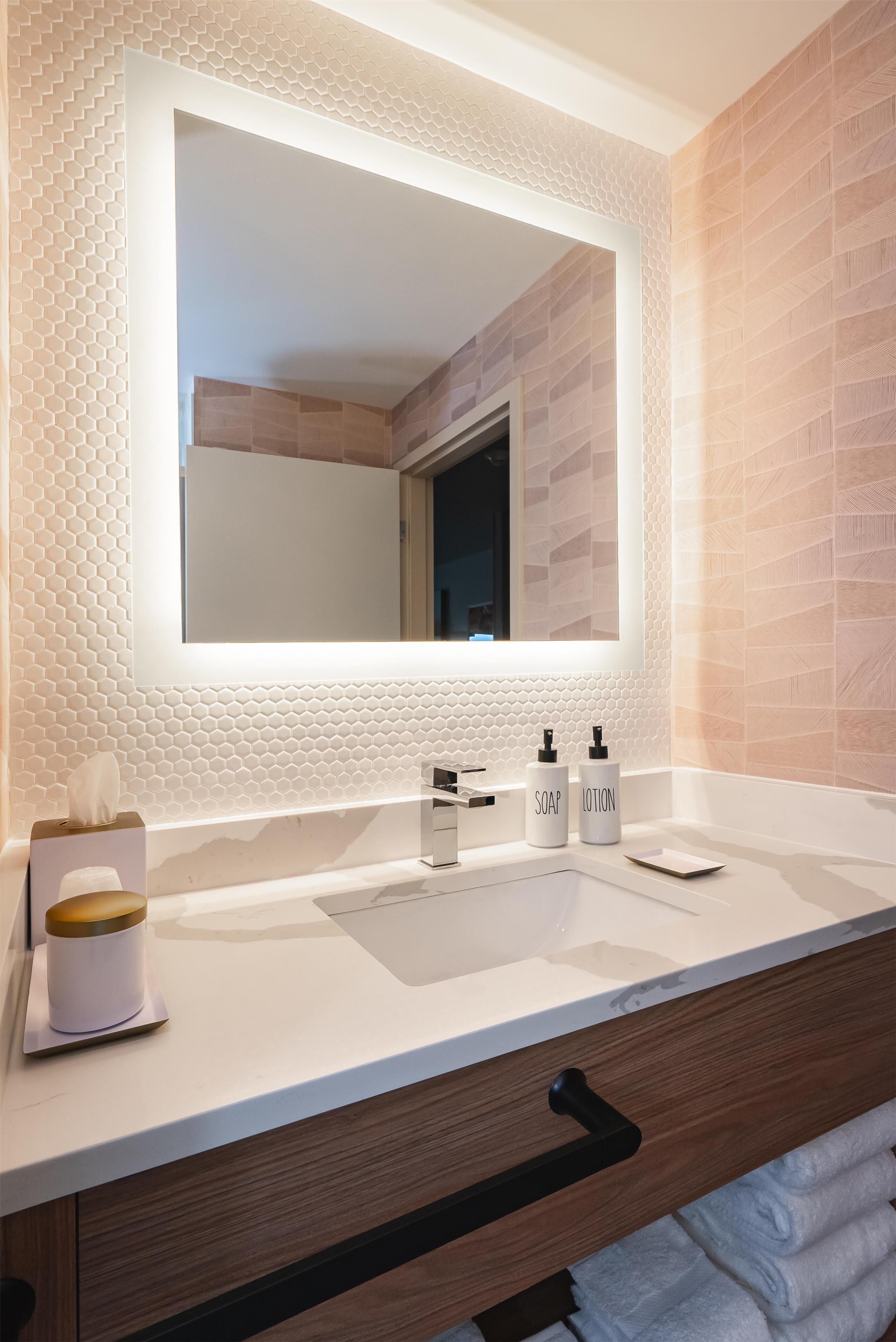 A bathroom with a large mirror, two bottles of soap and lotion, a tissue box, and a towel rack.