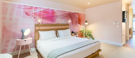 A bedroom with a large bed, a bedside table with a lamp, a wall mural, and a potted plant.