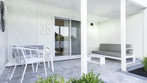 A modern outdoor seating area with a white sofa and a table, a sliding glass door, and a number '25' on the wall. - The Bentley Hotel Southampton (Southampton)