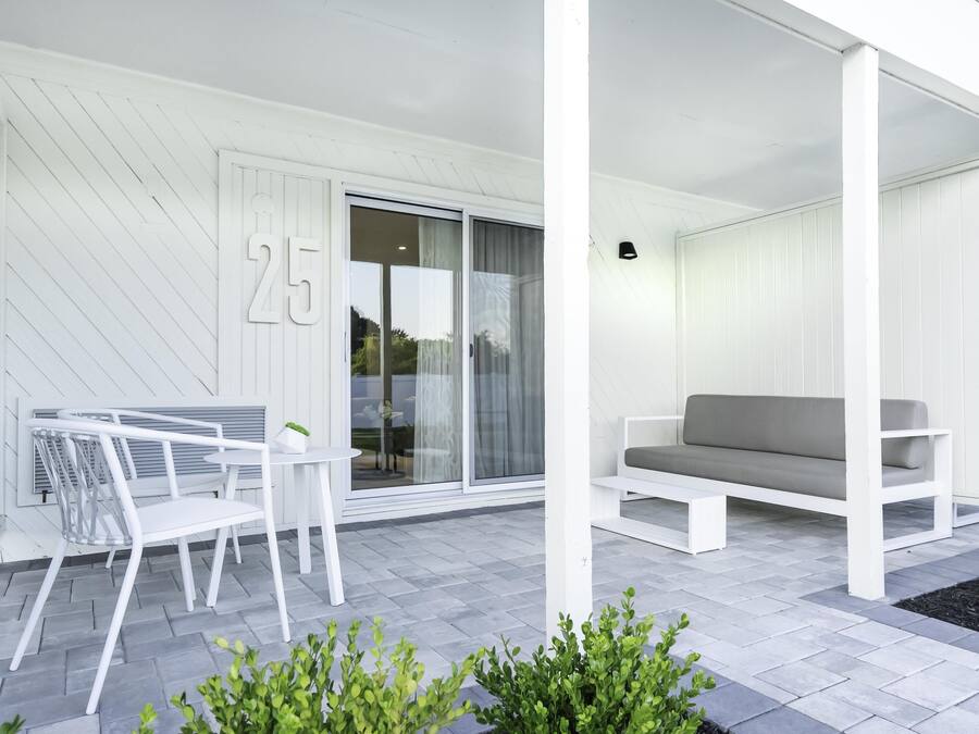 A modern outdoor seating area with a white sofa and a table, a sliding glass door, and a number '25' on the wall.