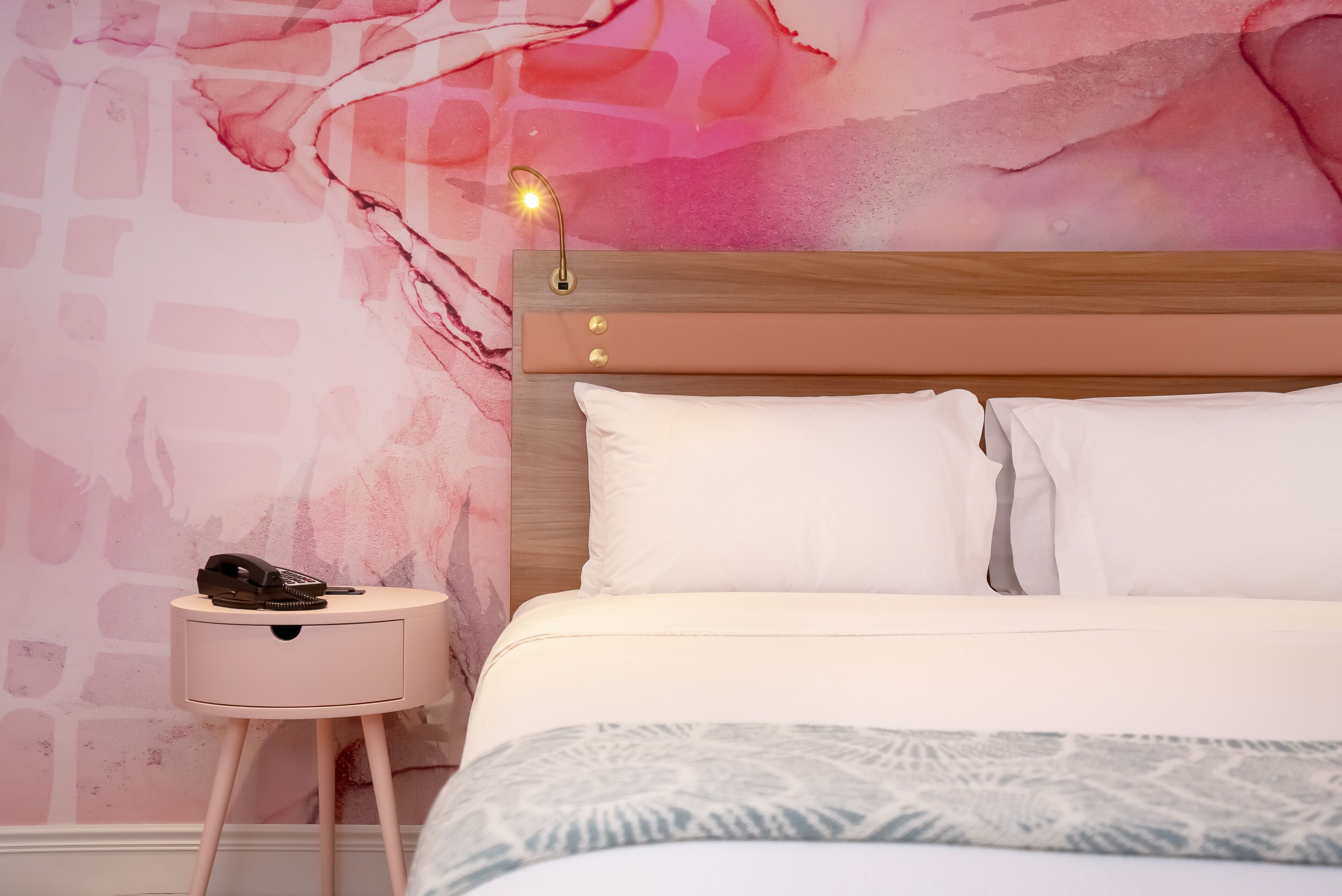 Una camera da letto con un letto, un comodino con una lampada e una parete decorata con un motivo astratto rosa.