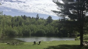 Rauhallinen paikka järven rannalla, jossa on nurmialue, kaksi Adirondack-tyylistä puutarhatuolia ja puu.