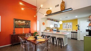 Een moderne keuken met een centraal eiland, een eethoek met transparante stoelen en een schilderij aan de muur.