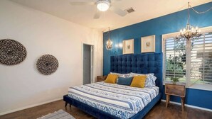 Een slaapkamer met een gestoffeerd hoofdeinde, een bed met een decoratief sprei en een kroonluchter.