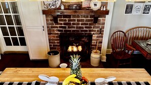 Un comedor con mantel a cuadros, un frutero y dos figuras decorativas de conejos. Al fondo, una chimenea de ladrillo con fuego encendido.