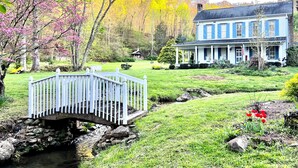 Una casa con un porche, un pequeño puente y un jardín lleno de flores.