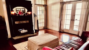 Una sala de estar con chimenea, un sofá de cuero rojo y un ventanal con cortinas.