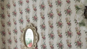 Ein Schlafzimmer mit floralem Wandpapier, einem hölzernen Bettgestell und einem Nachttisch mit Lampe.