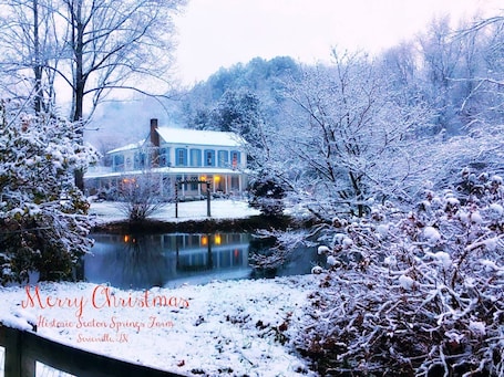 A historic Seaton Springs Farm with a large house and a pond, surrounded by snow-covered trees.